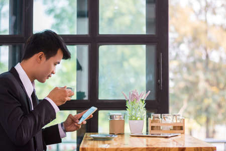 Young businessmen are looking at mobile phones and holding a cup of coffee.の写真素材