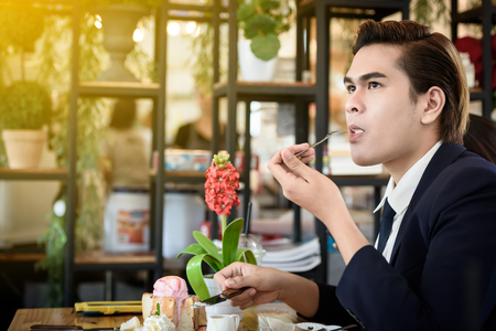 Asian businessman eating ice cream bread topped with honey on a wooden table in a coffee shop. Food, drinks and business concepts.の写真素材