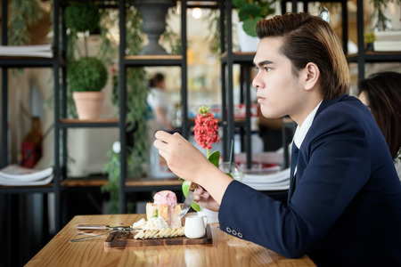 Asian businessman eating ice cream bread topped with honey on a wooden table in a coffee shop. Food, drinks and business concepts.の写真素材