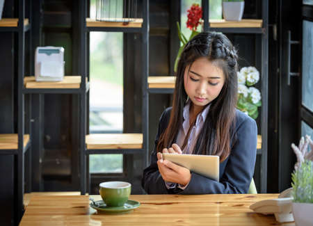 Beautiful Asian businesswoman is using tablet standing near window glass. Within the office. Technology and Business Communication Concept.の写真素材