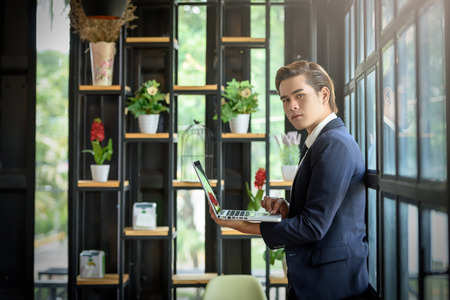 Businessmen are using a laptop computer standing near the window glass. Within the office. Technology and Business Communication Conceptの写真素材