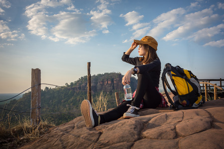 Tourist young woman wearing hat enjoying sitting and drink water on the mountain.