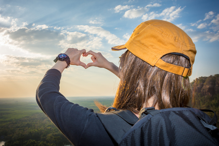 A tourist wearing a red hat is doing a heart-shaped hand on the mountain.の写真素材