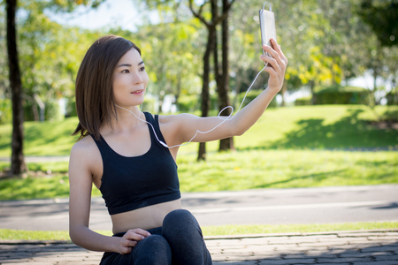 Girl sitting listening to music from a mobile phone and taking pictures during a workout session.の写真素材