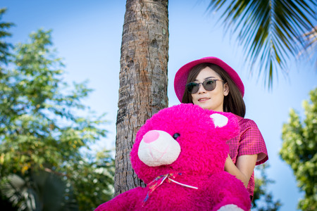 Girl hugging a teddy bear happily on the grass under the coconut.の写真素材
