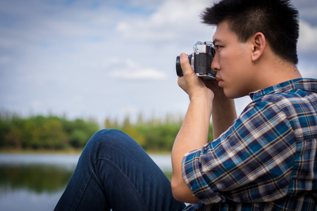 Hipster man sitting on the lake pier with holding vintage camera, Relaxed atmosphere, summer.の写真素材