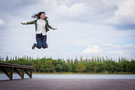 Woman jumps with arms raised on a bench by the pool.の写真素材