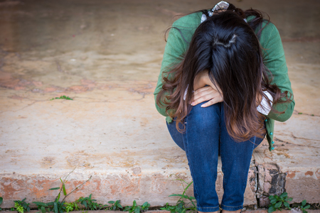 Depressed women. Asian beautiful girl sits sadly on the cement floor in ancient houses.の写真素材
