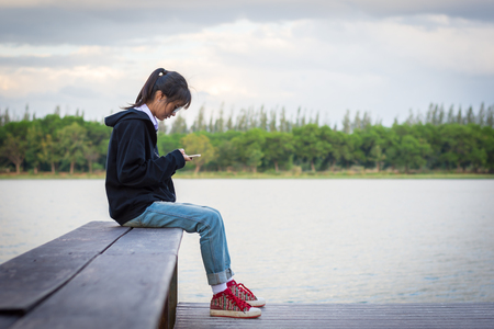 young woman is using a cell phone while sitting at the river.の写真素材