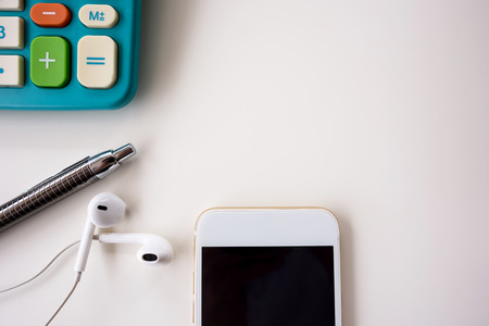 Work space top view with mobile phone and earphone on white wood table.