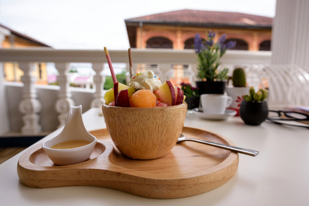Fruit ice cream in a wooden bowl with sweetened condensed milk in a white spoon on a white tableの写真素材