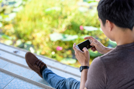 Hipster men playing games on the phone near the river.の写真素材