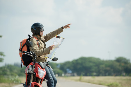 Travelers or backpackers are reading a map and pointing to destinations on a motorbike for travel.