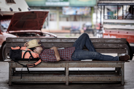 Bus station with Asian backpacker tourist sleeping on a bench waiting for a bus.の写真素材
