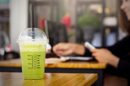 A cup of coffee on a wooden table in a coffee shop. Background is a business woman using a mobile phone.の写真素材