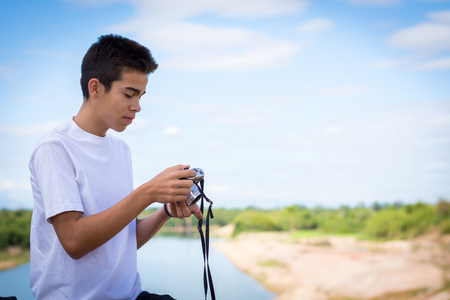 Young man with an old camera is sitting on a bridge.の写真素材