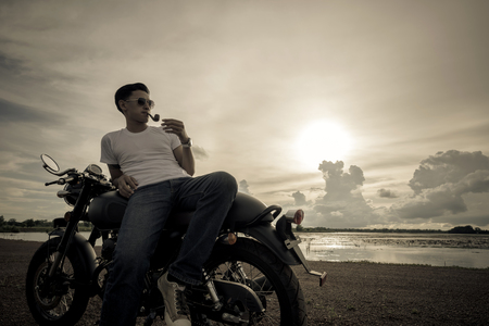 Motorcycle or motorbike with male rider is smoking and standing at the river.の写真素材