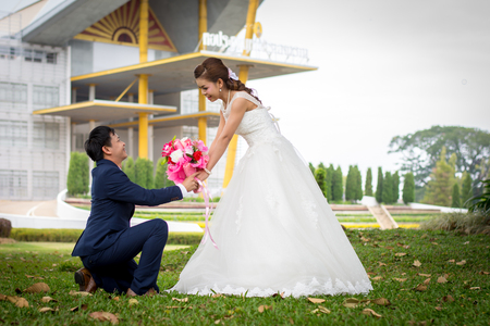 Beautiful Young wedding couple with white umbrellas sitting on a green lawn. Man gave flowers to young woman.の写真素材