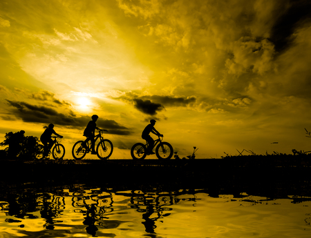 Silhouette The family are riding a bicycle, while the sunset.の写真素材