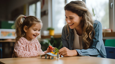A young girl and her mother are sitting at a table playing with toys. The girl is smiling and the mother is looking at her with love in her eyes.の素材