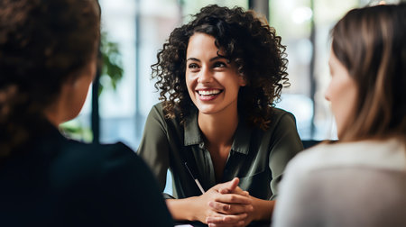 A young woman with curly hair is smiling and looking at someone while sitting at a table.の素材