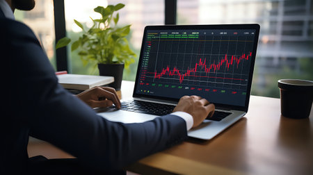A businessman in a suit is using a laptop to track stock prices.の素材