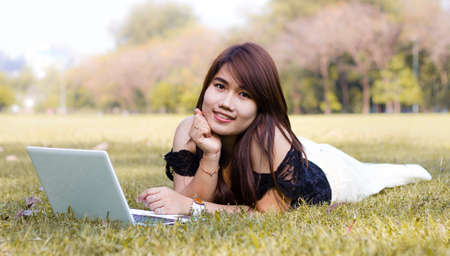 Young pretty woman with laptop lying in a parkの写真素材