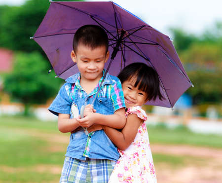 A smiling boy and a little girl with umbrella in the park の写真素材