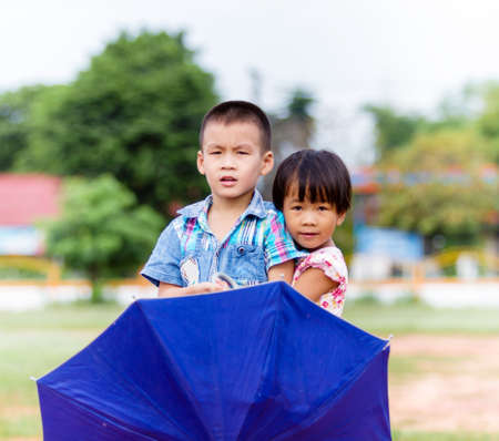 A smiling boy and a little girl with umbrella in the park の写真素材