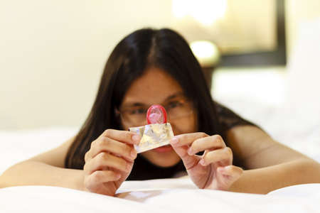 Asia woman opening a condom on her bed  Focus on the condom in the foreground  の写真素材