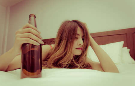 Drunk young on bed with bottle of beer in hand の写真素材
