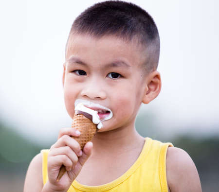 Asian caucasian boy enjoying a melting chocolate ice-cream on a sweltering hot summer day