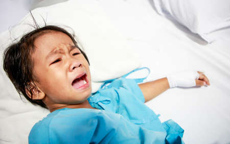 Sick little girl crying in hospital bedの写真素材