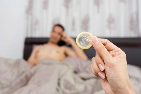 Woman showing a condom on bed, Focus on the condom in the foregroundの写真素材