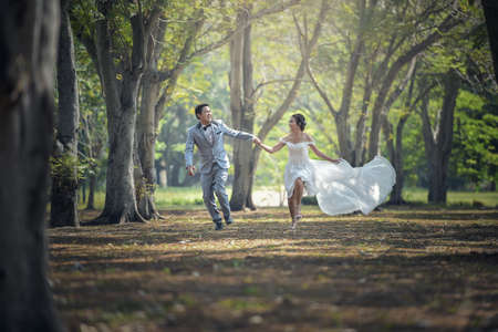 Bride and groom running and park and holding handsの写真素材