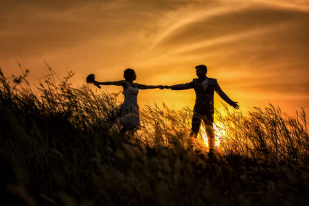 Just married loving hipster couple in wedding dress and suit on field at sunset. happy bride and groom in the summer meadow. Romantic Married young familyの写真素材