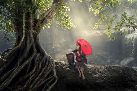 Asian young woman relaxing in nature. with red umbrella in green forest.の写真素材