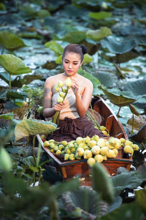 Asian woman in Thai rural traditional dress sitting on boat in the lotus garden at morningの写真素材