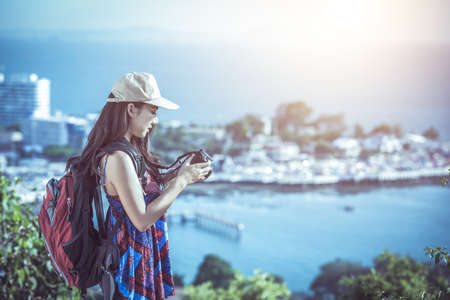 Beautiful young woman with long hair photographer takes a picture of a mountain landscape on the camera while hikingの写真素材