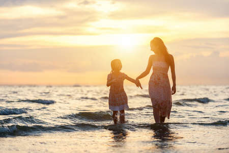 Mother and daughter having fun walking and playing on the beach at sunsetの写真素材