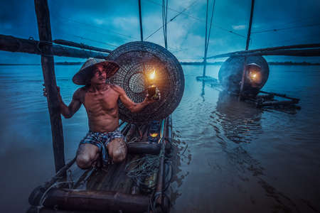 Asian fisherman holding a lantern on his boat waiting to fish in the Mekong. During the twilightの写真素材