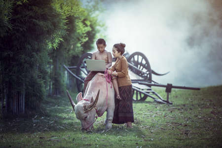 Happy boy and sister using a laptop outdoors On the buffalo, Countryside of Thailand, ASIAの写真素材