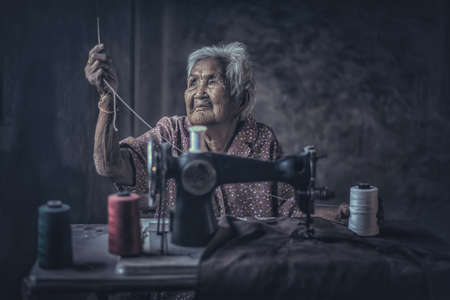 Cute 90 year old senior woman using vintage sewing machine. adorable elderly woman sewing clothes in her old family home.の写真素材
