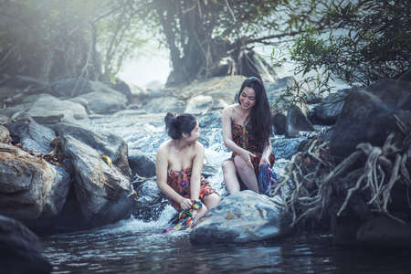 Asian women washing clothes at the creek the traditional way of life with a beautiful nature, the countryside of Thailandの写真素材