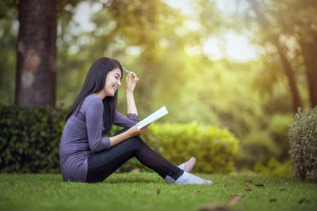 Portrait of happy charming  Asian woman reading a book outdoorsの写真素材