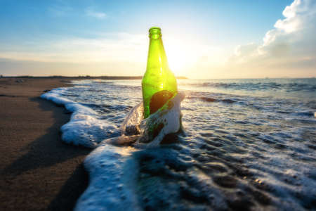 Beer bottle on a sandy beach with clear sky and waveの写真素材