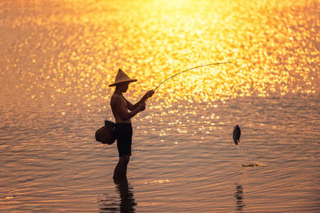 Boy is fishing at sunset on the lakeの写真素材