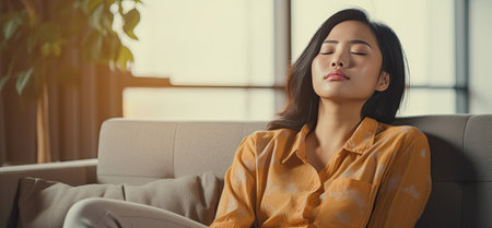 Asian woman resting at home on couch, feeling exhausted after work, lacking energy, or overworked, too tired, and lacking motivationの素材