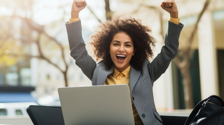 A businesswoman celebrates with her arms up while looking a laptop in a happy and successful poseの素材