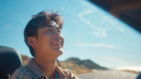 A young Asian man drives a car on a clear day. With beautiful blue sky. He smiling driving to travel by car. Sticking her head outta the windshieldの素材